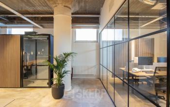 Modern office space with glass partitions, concrete floors, and a potted plant at Brouwerijstraat 1, in Enschede. Available for office space rental.