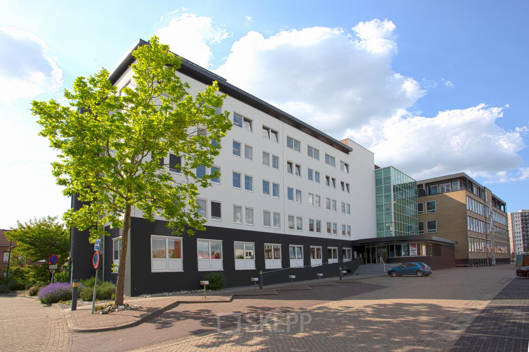 Exterior view of a modern office building, located at Brouwerijstraat 1, Enschede, featuring a clean white facade with black accents and large windows. Ideal for office space rental with ample light and contemporary design.