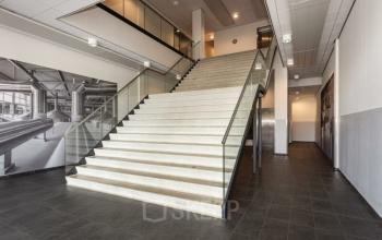 Interior view of a modern office building at Brouwerijstraat 10, Enschede, featuring a spacious entrance with a wide staircase and sleek design. Ideal for office space rental purposes.
