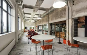 Spacious and modern office space rental at Brouwerijstraat 10, Enschede, with high ceilings, large windows, and contemporary furnishings, including tables and chairs for collaborative work.