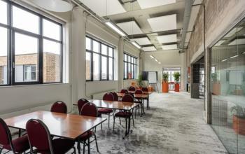 Spacious office to rent at Brouwerijstraat 10, Enschede with large windows, modern lighting, and multiple tables with chairs.
