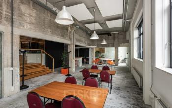 Interior view of office space at Brouwerijstraat 10, Enschede, featuring wooden tables, red chairs, and industrial-style decor with concrete walls.