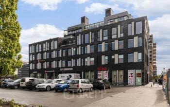 Exterior view of the office building located at Brouwerijstraat 10, Enschede, featuring parking space in front and various retail stores on the ground floor.