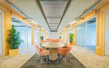 Bright and inviting office space rental in Enschede featuring a long table with chairs, surrounded by glass-partitioned areas and greenery.