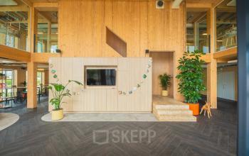 Inviting office space with wooden accents, indoor plants, and a display area at Moutlaan 1-23, Enschede, perfect for office space rental.