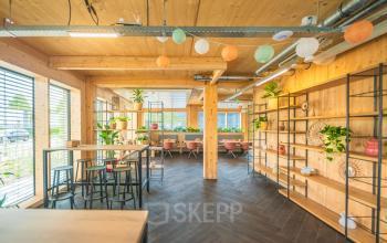 Bright, wooden-accented office space in Enschede featuring high tables and seating areas, ideal for office space rental. Abundant natural light and greenery enhance the ambiance.