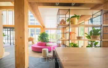 Bright, modern office space at Moutlaan 1-23, Enschede with wooden beams, vibrant seating, and open shelving. Ideal office space rental for dynamic work settings.