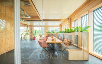 Bright and stylish office space at Moutlaan 1-23, Enschede, featuring glass walls, wooden accents, and modern furniture. Office space rental available with scenic views.