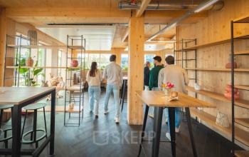 Modern office space at Moutlaan 1-23, Enschede, featuring stylish wooden interiors with shelves and high chairs, ideal for office space rental. A group of people discusses business strategies.