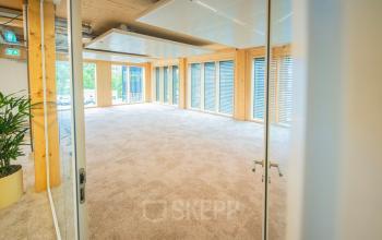 Spacious office area at Moutlaan 1-23 in Enschede, ideal for rent. Bright and airy with large windows and modern wood accents.