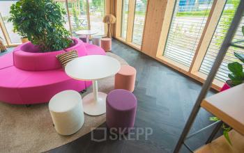 Bright office space at Moutlaan 1-23, Enschede featuring colorful seating, round tables, and large windows, perfect for rent office space with a modern touch.