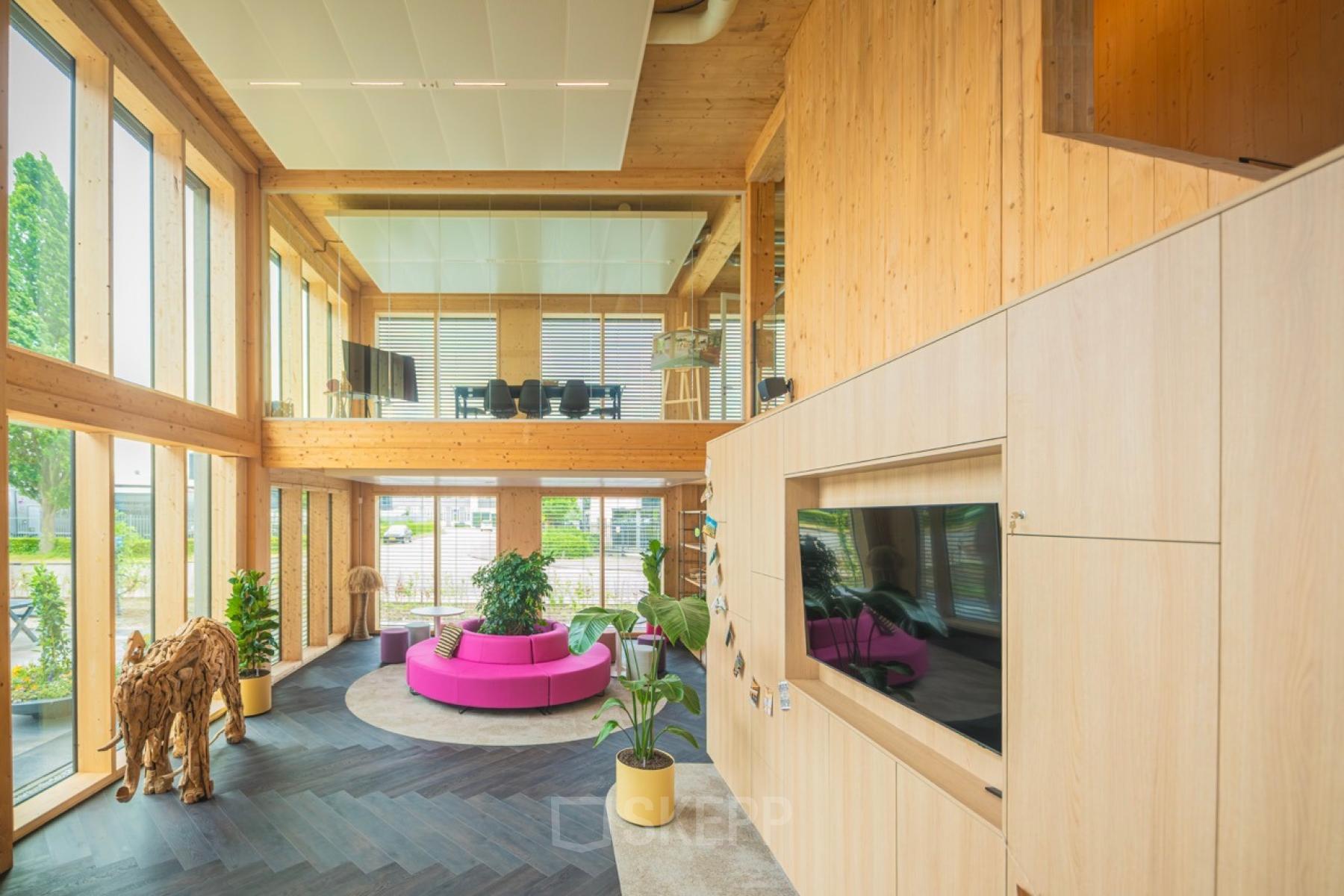 Bright, spacious office space at Moutlaan 1-23, Enschede, featuring a stylish interior with natural wood elements, modern furniture, and large windows enhancing the ambiance. Suitable for rent office space needs.