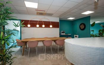 Furnished office at Boddenkampsingel 95 in Enschede with a long wooden table, pink chairs, and a dartboard, available for office space rental.