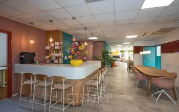Bright office space to rent at Boddenkampsingel 95, Enschede, featuring a furnished interior with a long table, bar stools, and colorful decor, ideal for workspaces.
