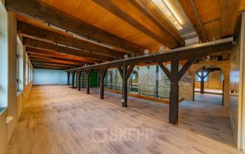 Spacious open office space with wooden beams and carpeted flooring at Prins Hendrikkade 3, ideal for office space rental in Franeker.