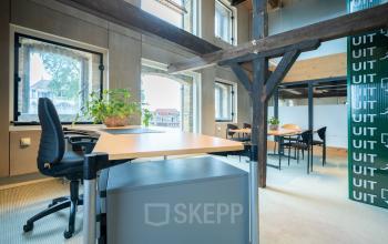 Office space rental at Prins Hendrikkade 3, Franeker, featuring multiple workspaces with desks and chairs, natural light from large windows, and industrial beams.