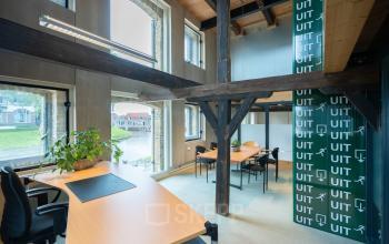 Bright office space at Prins Hendrikkade 3, Franeker, featuring large windows and wooden beams, with desks and chairs for rent. Ideal for office space rental.