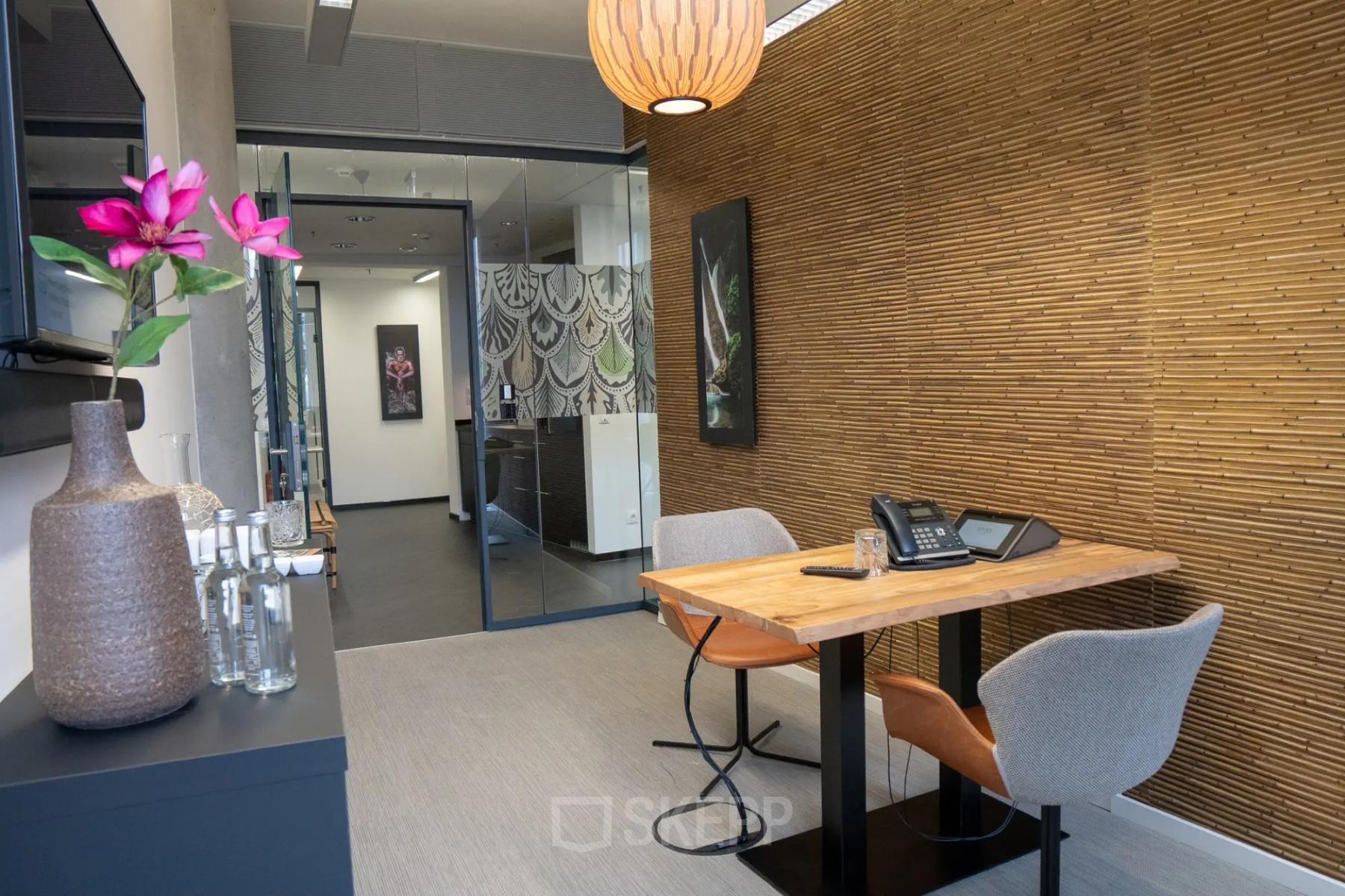 Büroraum mit Holztisch und zwei Stühlen in Baseler Straße 10, Frankfurt Hauptbahnhof. Dekor an der Wand und Glaswand im Hintergrund.