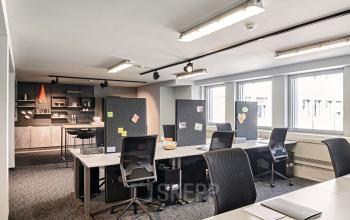 Modernes Büro in der Barckhausstraße 1, Frankfurt Westend mit mehreren Schreibtischen und Trennwänden, großem Fenster, und einem naheliegenden Kantinenbereich. Ideal, um einen Büroraum zu mieten.