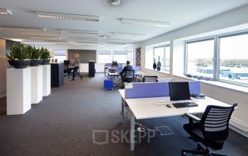 Spacious open office at Transportlaan 1-151, Geleen, featuring modern desks and large windows; people engaged in various business activities. Ideal for office space rental.