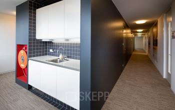 Bright hallway in office space rental with built-in kitchenette, featuring sleek black and white cabinetry in Geleen.