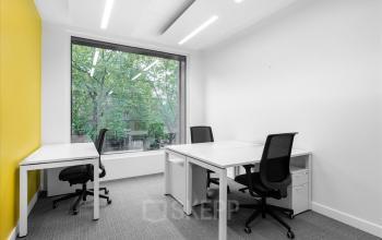 Helles Büro zur Miete in der Rue de Lyon 77, Genf Les Charmilles, mit weißen Tischen und schwarzen Bürostühlen vor einem großen Fenster.