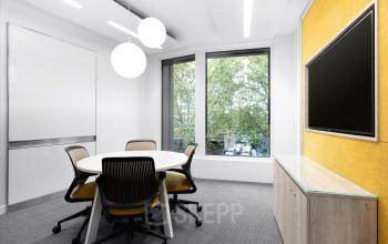 Modernes Büro in der Rue de Lyon 77, Genf Les Charmilles, mit einem runden Tisch und fünf Stühlen vor einem großen Fenster.