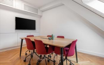 Modern gestalteter Büroraum mieten in Genf Innenstadt, Place de la Fusterie 12, mit Holztisch und roten Stühlen vor einem Flachbildschirm an der Wand.