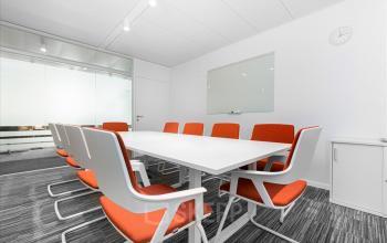 Moderne Bürofläche mieten in Genf Innenstadt, Rue du Commerce 4, mit weißem Konferenztisch und orangefarbenen Stühlen.