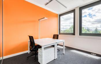 Modern eingerichtetes Büro zum Mieten in Genf Meyrin, Route de Pre-Bois 14, mit hellem Raum und orange Akzentwand.