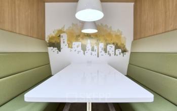 Moderne Sitzecke für Meetings im Büro in Place Casa-Bamba 1-3, Genf Vernier mit grünen Polsterbänken und stilvollem Wandbild.