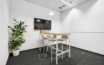 Moderner Büroraum in der Route de Meyrin 123 in Genf Vernier, ideal um Bürofläche zu mieten. Ausgestattet mit einem hohen Tisch, Stühlen, Monitor und Pflanzen für Besprechungen.