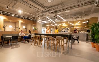 Bedrijvige kantoorlounge aan de Gaston Crommenlaan 8 in Gent Ledeberg, waar mensen samenwerken en ontspannen. Diverse zitmogelijkheden en een moderne bar aanwezig. Kantoorruimte te huur voor professionals.