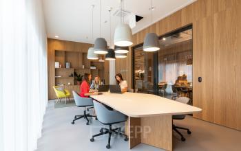 Modern kantoor te huur op Gaston Crommenlaan 8, Gent Ledeberg, met houten wanden, vergadertafel en kantoormeubilair. Mensen overleggen rond de tafel.