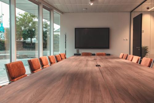 Modern conference room with a large wooden table, orange chairs, and a large TV screen, located at Oktrooiplein 1 in Ghent, available for office space rental.