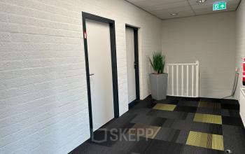 Interior hallway of an office building at Techniekweg 15, Gorinchem, featuring carpeted floors, white brick walls, and potted plant.