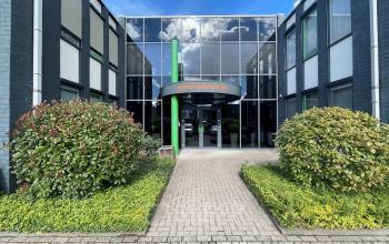 Entrance of the office building at Techniekweg 15, Gorinchem with glass doors and manicured bushes.