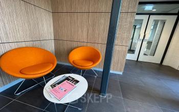 Modern office lobby at Techniekweg 15, Gorinchem featuring vibrant orange chairs and a small table, perfect for welcoming clients. Ideal for office space rental.