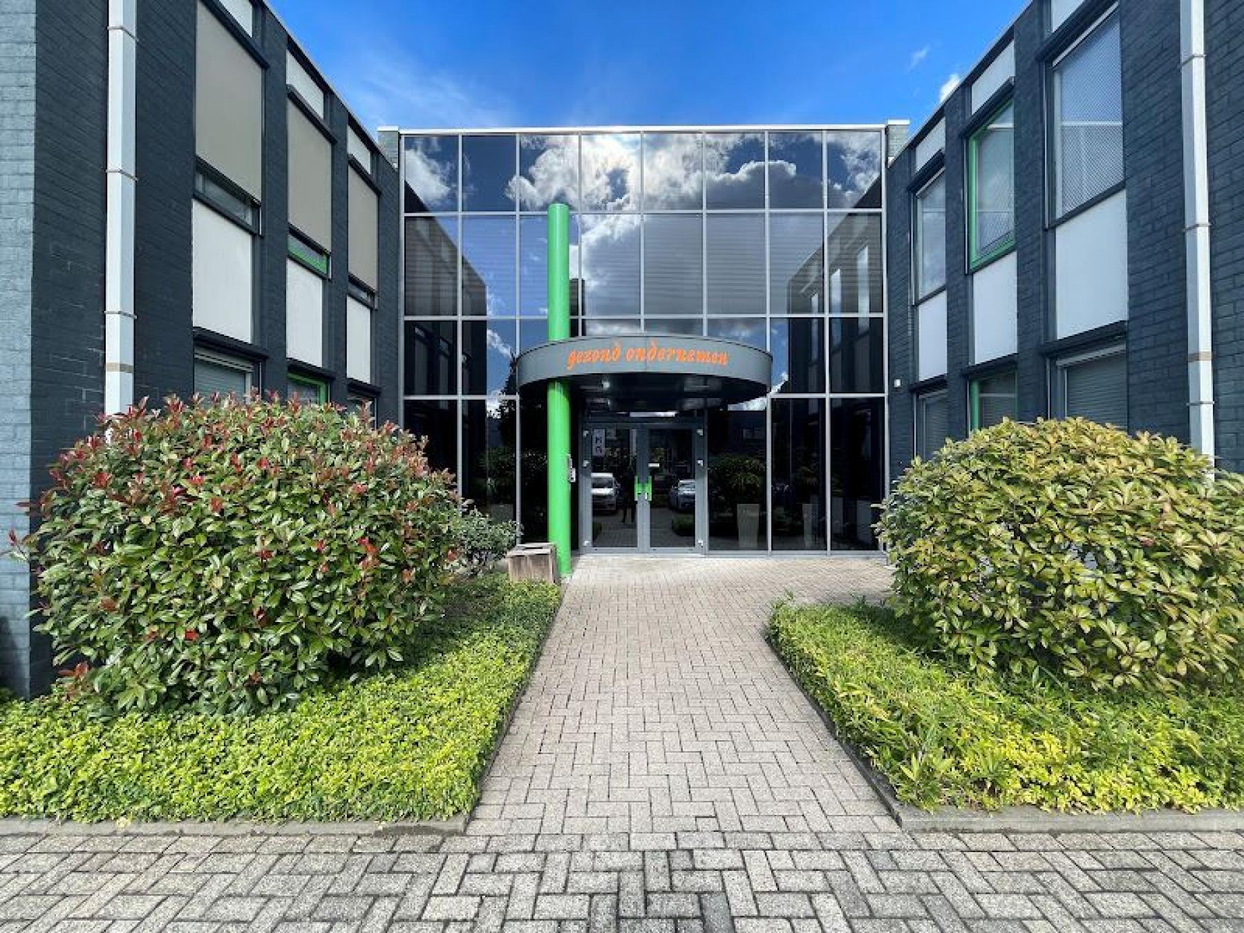 Entrance of the office building at Techniekweg 15, Gorinchem with glass doors and manicured bushes.