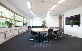 Bright office space to rent at Groningenweg 8 8, Gouda, featuring a modern conference room with a large table, chairs, wall-mounted screen, and potted plants by the window.