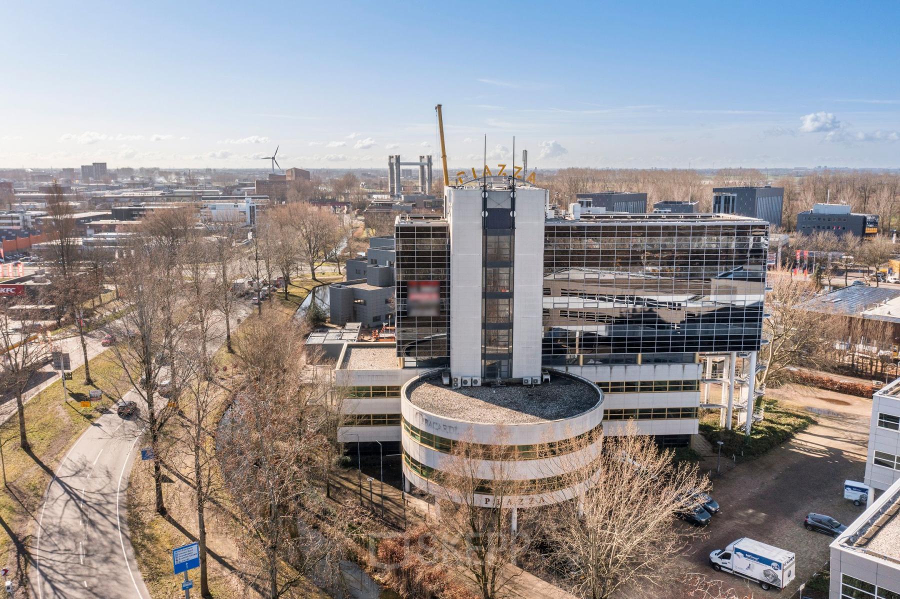 Exterior view of the office building at Groningenweg 8 8, Gouda, available for office space rental. The building is surrounded by trees and neighboring buildings.