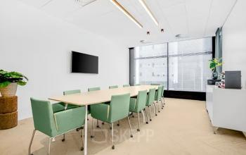Modern conference room with a long table and green chairs available for office space rental at Brückenkopfgasse 1, Graz.