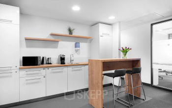 Modern Graz office space rental at Brückenkopfgasse 1 with white kitchenette, wooden bar stools and fresh flowers