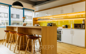 Modern office space rental at Waagner-Biro-Straße 47 in Graz with a vibrant pantry area featuring wooden furnishings and accent lighting.