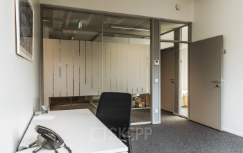 Modern Graz office space rental at Waagner-Biro-Straße 47 with a sleek desk, comfortable chair, and glass partition walls.