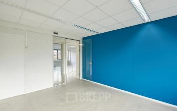 Bright empty office space with a blue accent wall and large windows in Groningen, ideal for office space rental at Schweitzerlaan 12.