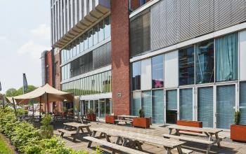 Exterior view of the office at Helperpark 270-298, Groningen, featuring wooden picnic tables outside a modern building. Ideal for businesses seeking office space rental in a contemporary setting.