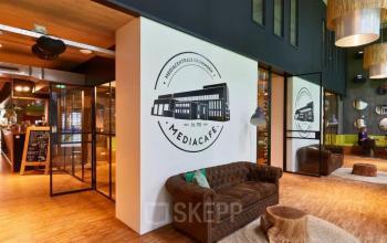 Inviting office space at Helperpark 270-298, Groningen featuring a cozy lounge with plush seating and stylish decor, ideal for meetings in this office space rental. Natural light illuminates the room through large windows.