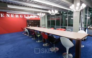 Modern office lounge area at Helperpark 270-298, Groningen, with long table, colorful chairs, and contemporary lighting, ideal for informal meetings.