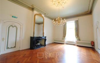 Elegant office space for rent at Staten Bolwerk 1 with high ceilings, large mirror, ornate chandelier, and parquet wood flooring.